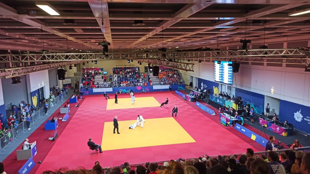 Blick auf zwei Judomatten in einer Halle. Auf beiden Matten finden Kämpfe statt.